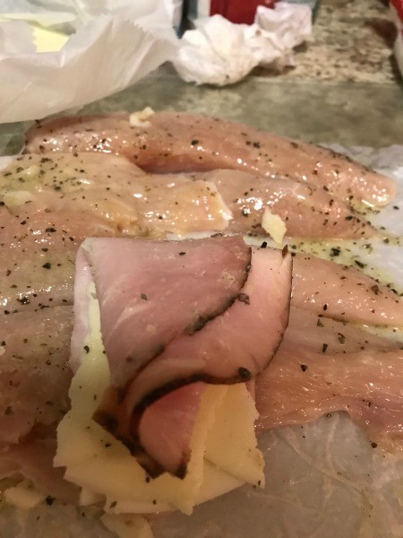 Rolling up the ham, cheese and chicken stack.
