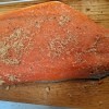 An uncooked salmon filet with seasonings on a cedar plank.