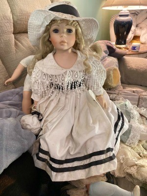 A porcelain doll in a white dress with a double stripe at the hem.