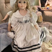 A porcelain doll in a white dress with a double stripe at the hem.