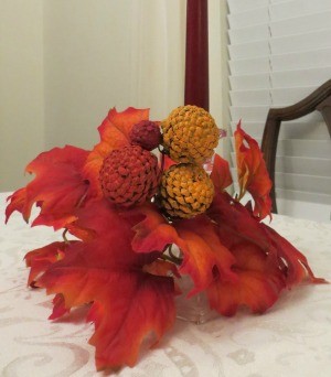 A candle arrangement with fall leaves and painted pinecone zinnias.