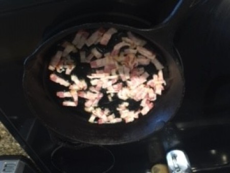 Cooking bacon pieces in a frying pan.