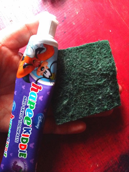 A tube of toothpaste and a green scrubby pad.
