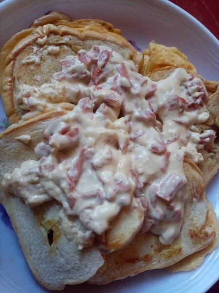 Putting the cheese sauce on top of the sandwich.