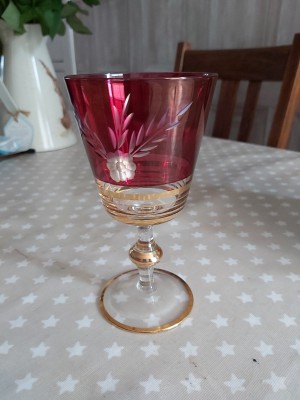 A footed glass with cranberry coloring and gold trim.