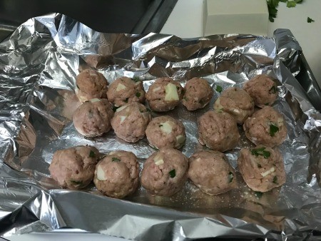 Several uncooked meatballs on aluminum foil.