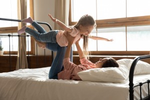 A mom flying her child above her on a bed.