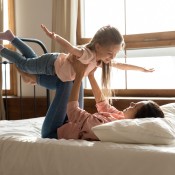 A mom flying her child above her on a bed.