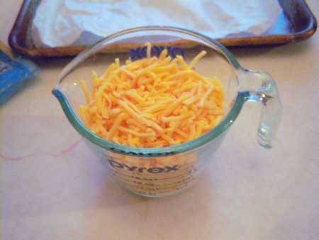 A measuring cup of shredded cheddar cheese.