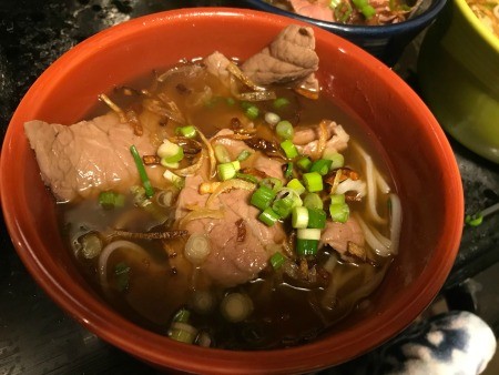 Adding green onions and crispy shallots to the bowl.