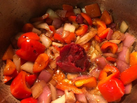Adding tomato paste to a large pot of vegetables.