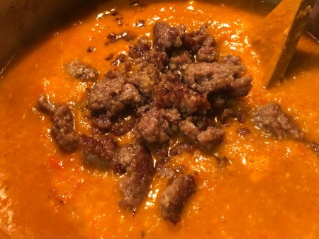 Adding the cooked sausage to the soup.