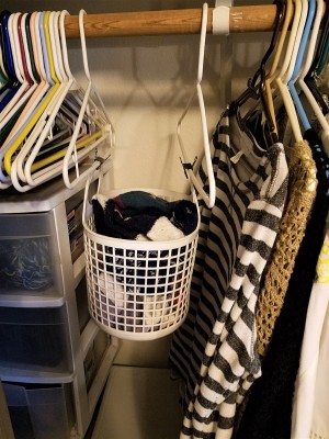 A basket hanging from two hangers in the closet.