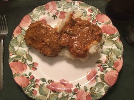 A plate of creamy pork chops over mashed potatoes.