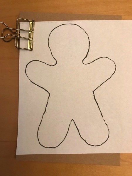 A tracing of a gingerbread man on a white sheet of paper.