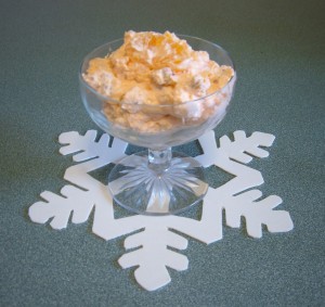 A footed glass bowl of orange pineapple fluff.