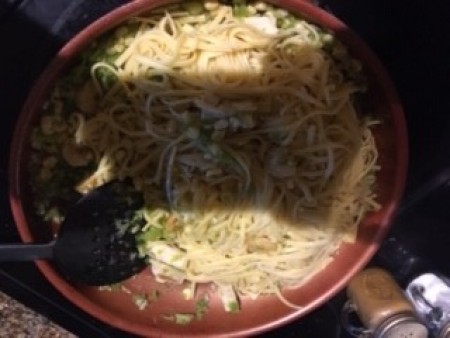 Adding cooked spaghetti noodles to the mixture.