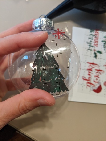 A clear ornament with a Christmas tree decal.