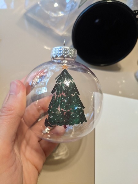 A clear ornament with a Christmas tree decal.