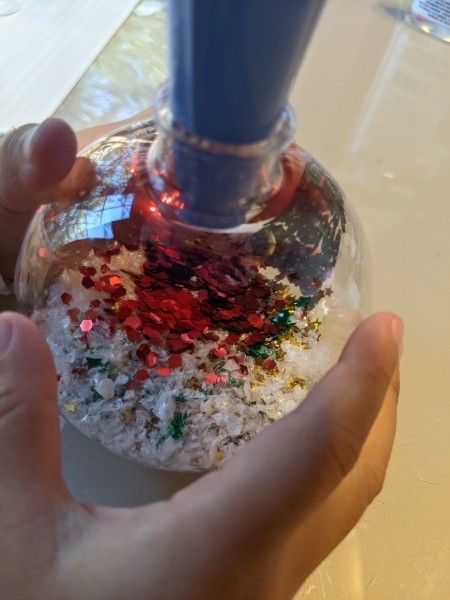 Funnelling glitter into a clear ornament.