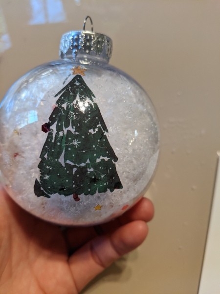 A clear ornament with snow and glitter with a Christmas tree decal.