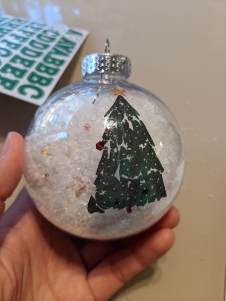 A clear ornament with snow and glitter with a Christmas tree decal.