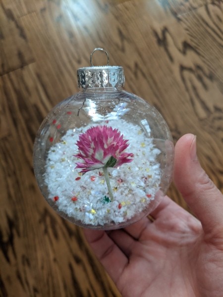 A clear ornament with snow and glitter inside and flowers outside.