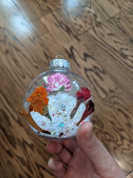 A clear ornament with snow and glitter inside and flowers outside.