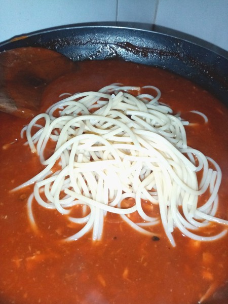 Adding pasta into the sauce.