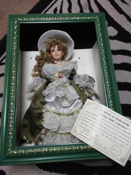 A doll in a shadowbox frame with a certificate.