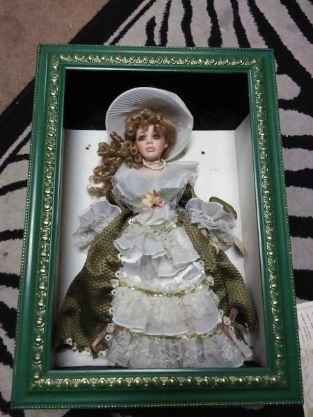A doll in a shadowbox frame.