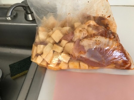 Adding potatoes and chicken to a plastic bag full of seasonings.