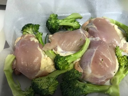 A baking sheet with chicken thighs and broccoli.
