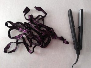 A hair flat iron next to a wrinkled ribbon.