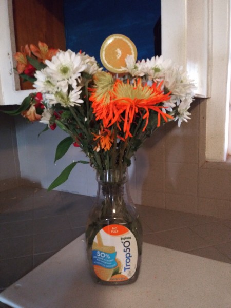 A plastic orange juice container being used as a vase.