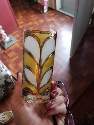 A decorative drinking glass in yellow and white with gold trim.