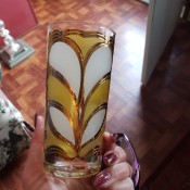 A decorative drinking glass in yellow and white with gold trim.