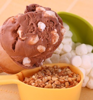 A scoop of rocky road ice cream next to marshmallows and nuts.