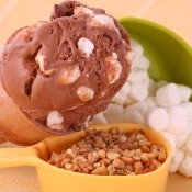 A scoop of rocky road ice cream next to marshmallows and nuts.