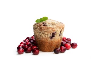 A cranberry muffin next to fresh cranberries.