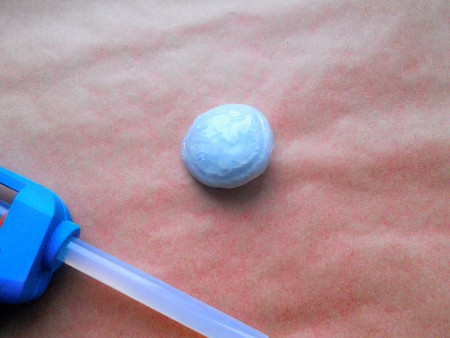 Making Shank Buttons the Cheap Way Using Concrete - button covered with hot glue, gun in the lower left