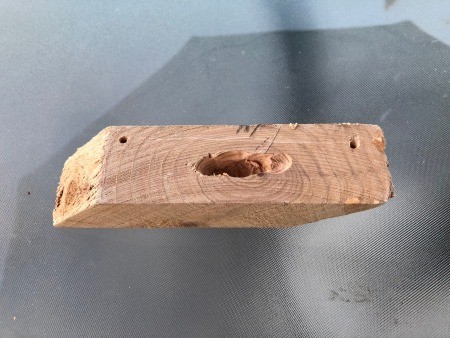 An angled piece of wood with a hole drilled in the middle.