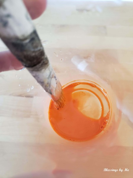 Putting a paintbrush in orange paint.