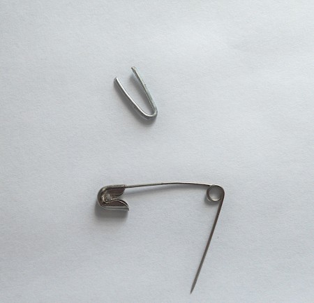 A small bent piece of metal next to a safety pin.