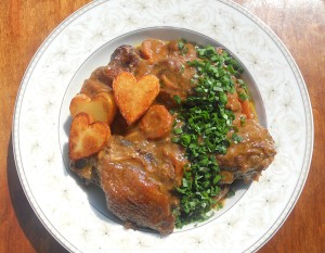 A plate of coq a vin with fried potatoes.
