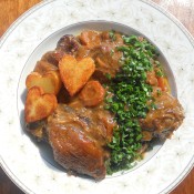 A plate of coq a vin with fried potatoes.