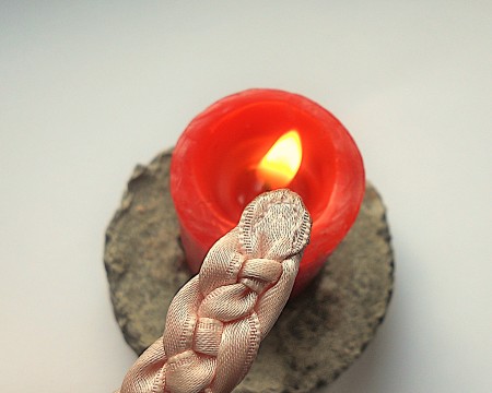 Finishing the ends of a ribbon belt with a candle flame.