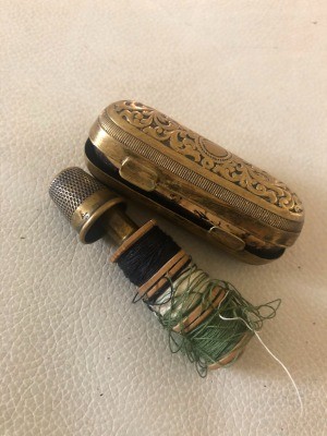 A silver thimble case with a thimble and thread holder.