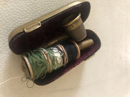 A silver thimble case with a thimble and thread holder.