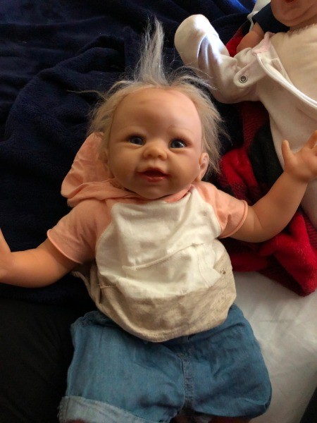 A baby doll with blonde hair and pink and white shirt.